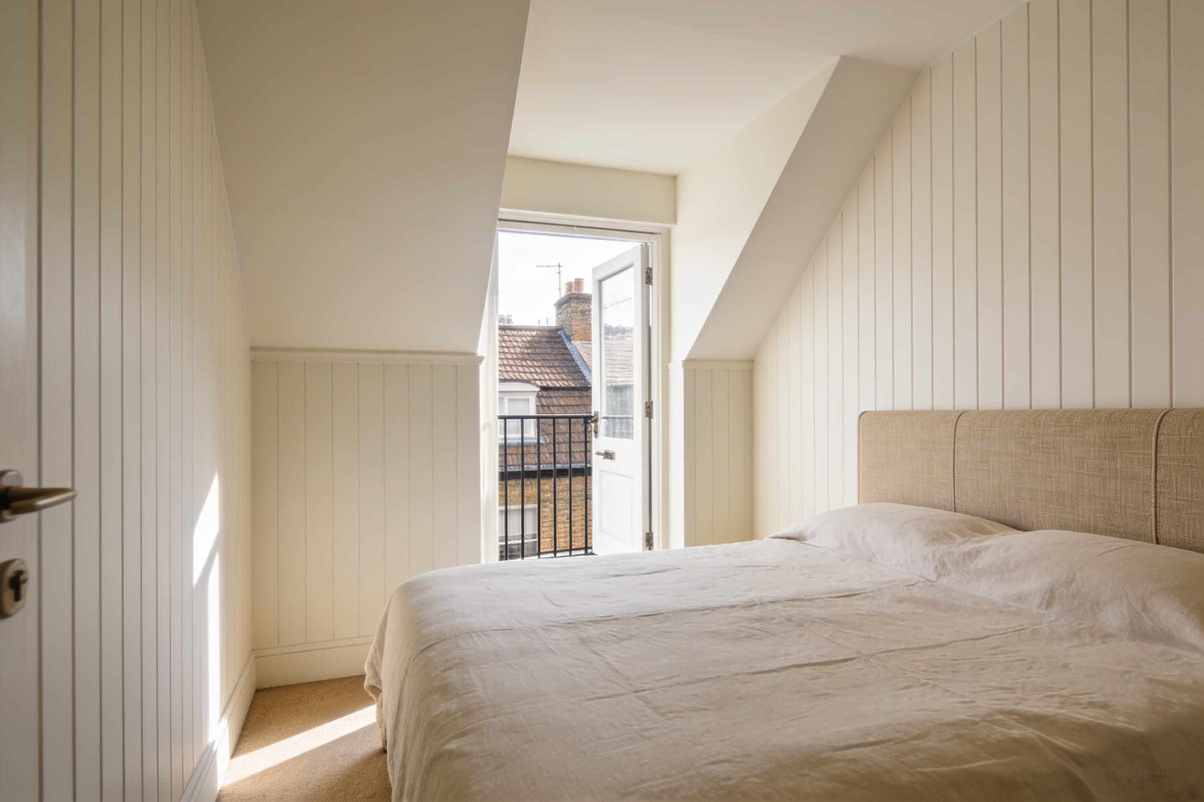 The main bedroom with a panelled wall and a small balcony door.
