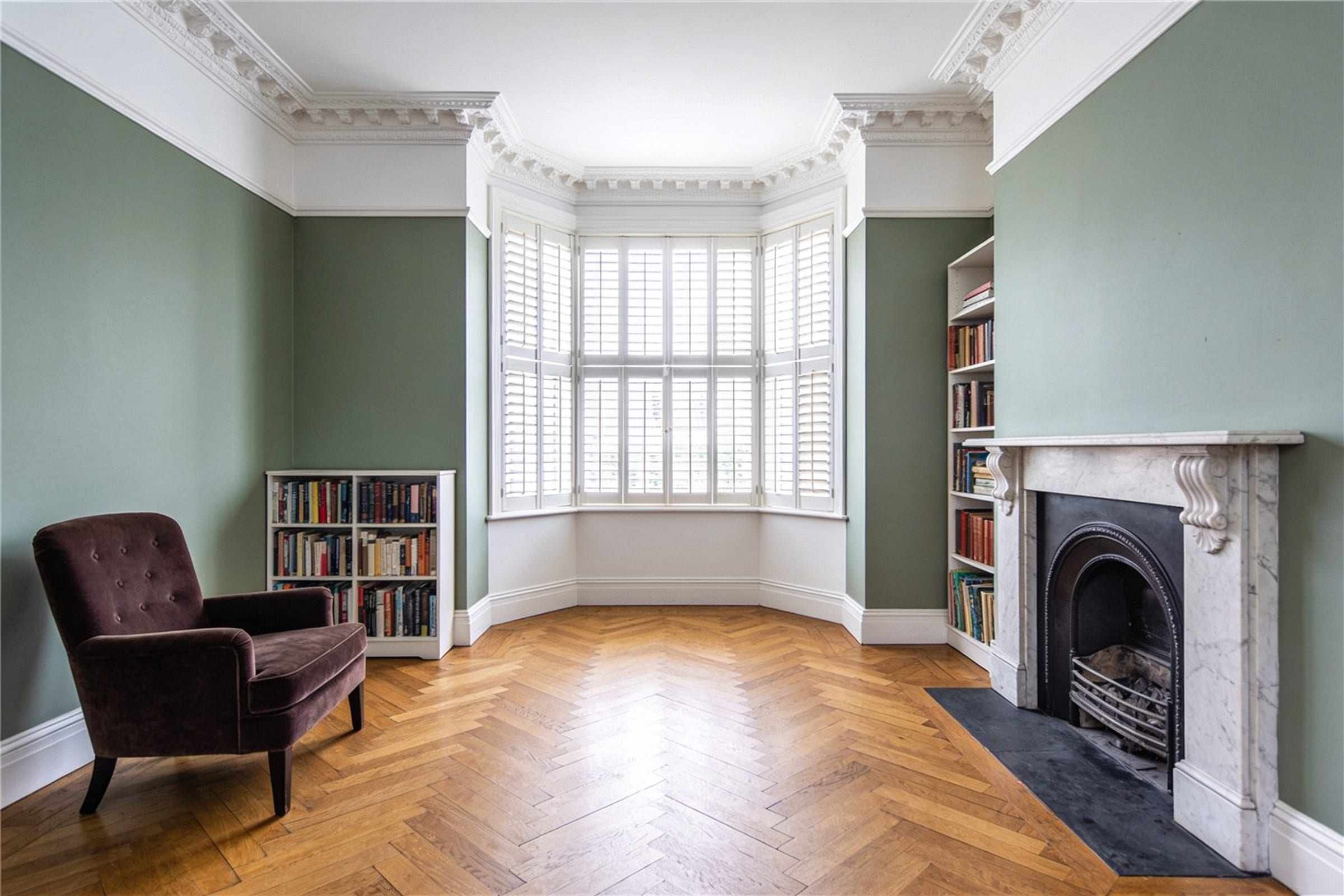 The sitting room with a marble fireplace, a shuttered bay window and sage green walls.