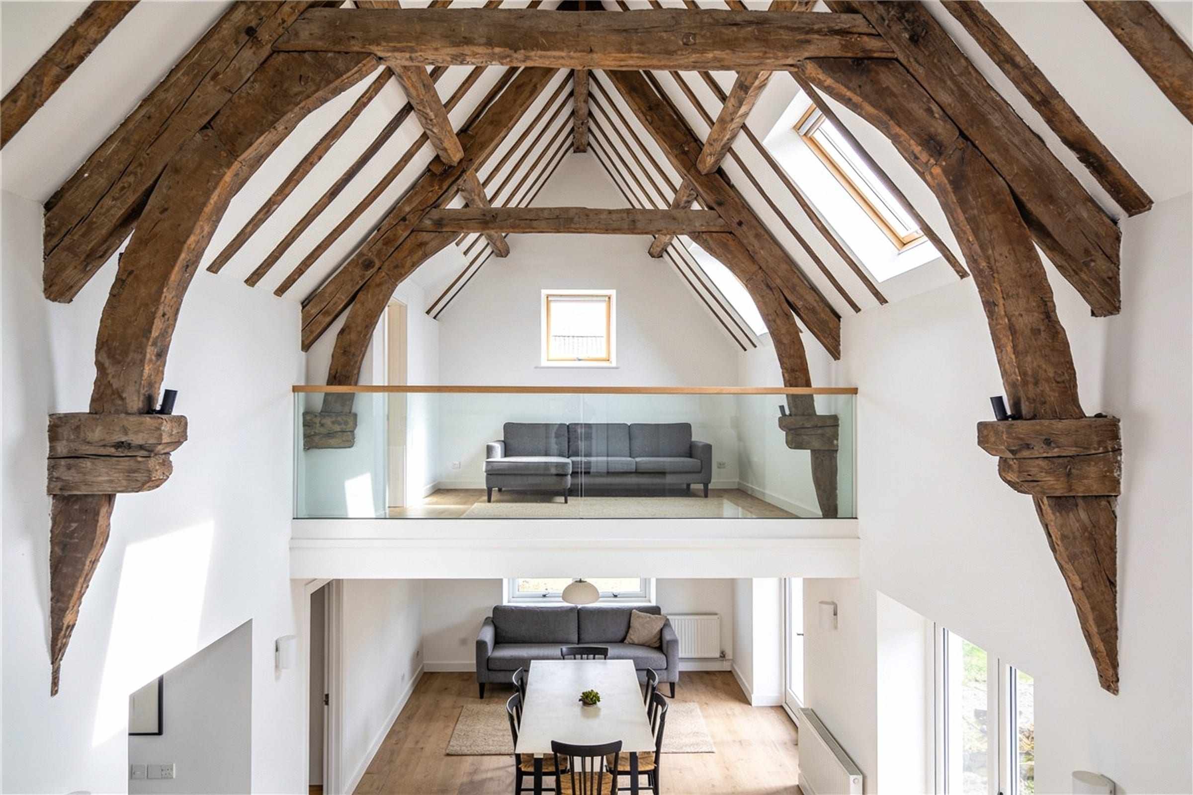 The living space under old timber trusses, with a mezzanine and a glass balustrade.