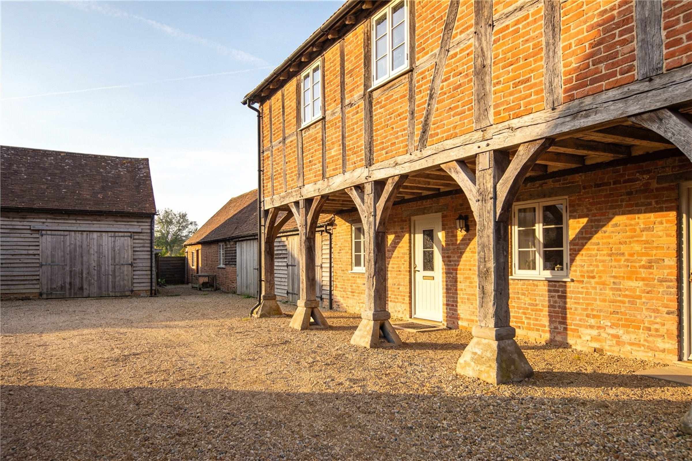 A restored brick and timber granary on staddle stones in a gravel farmyard of converted barns.