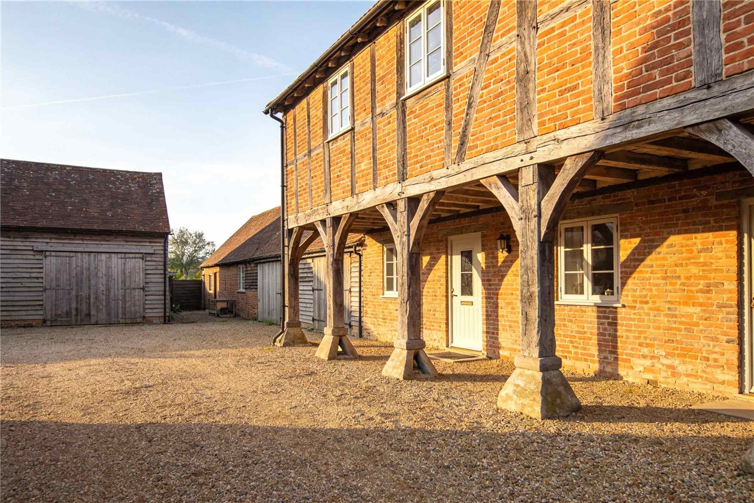 A restored brick and timber granary on staddle stones in a gravel farmyard of converted barns.