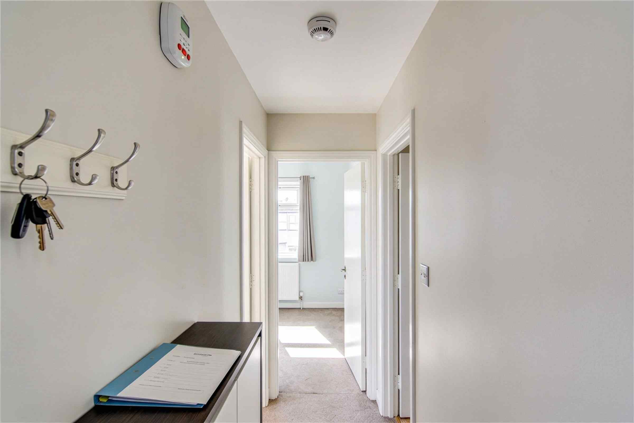 A tidy rented hallway with a smoke alarm on the ceiling, keys on a hook and a folder on a console table.